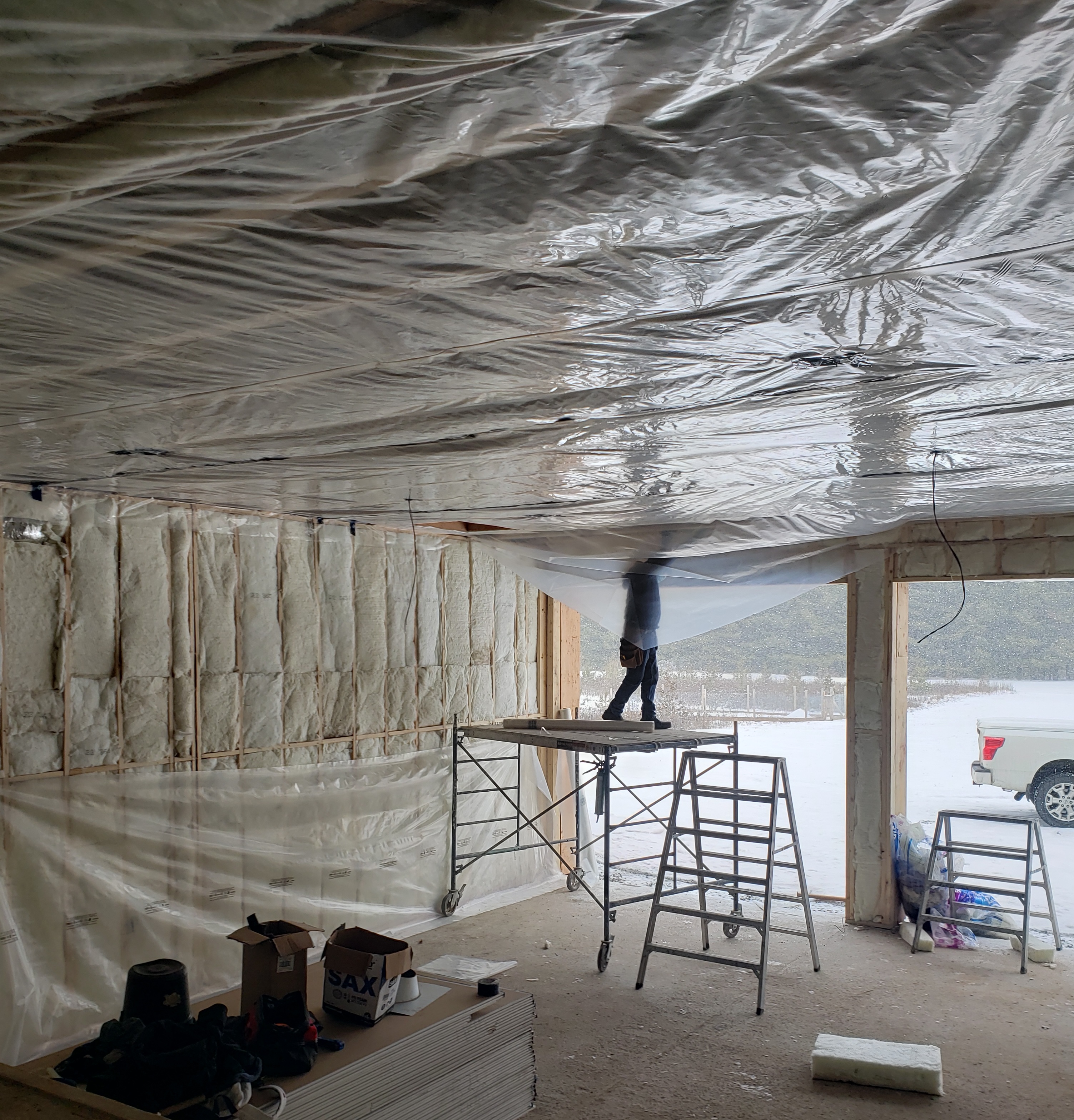 An open garage under construction showing a worker installing insulation with a mountain in the background.