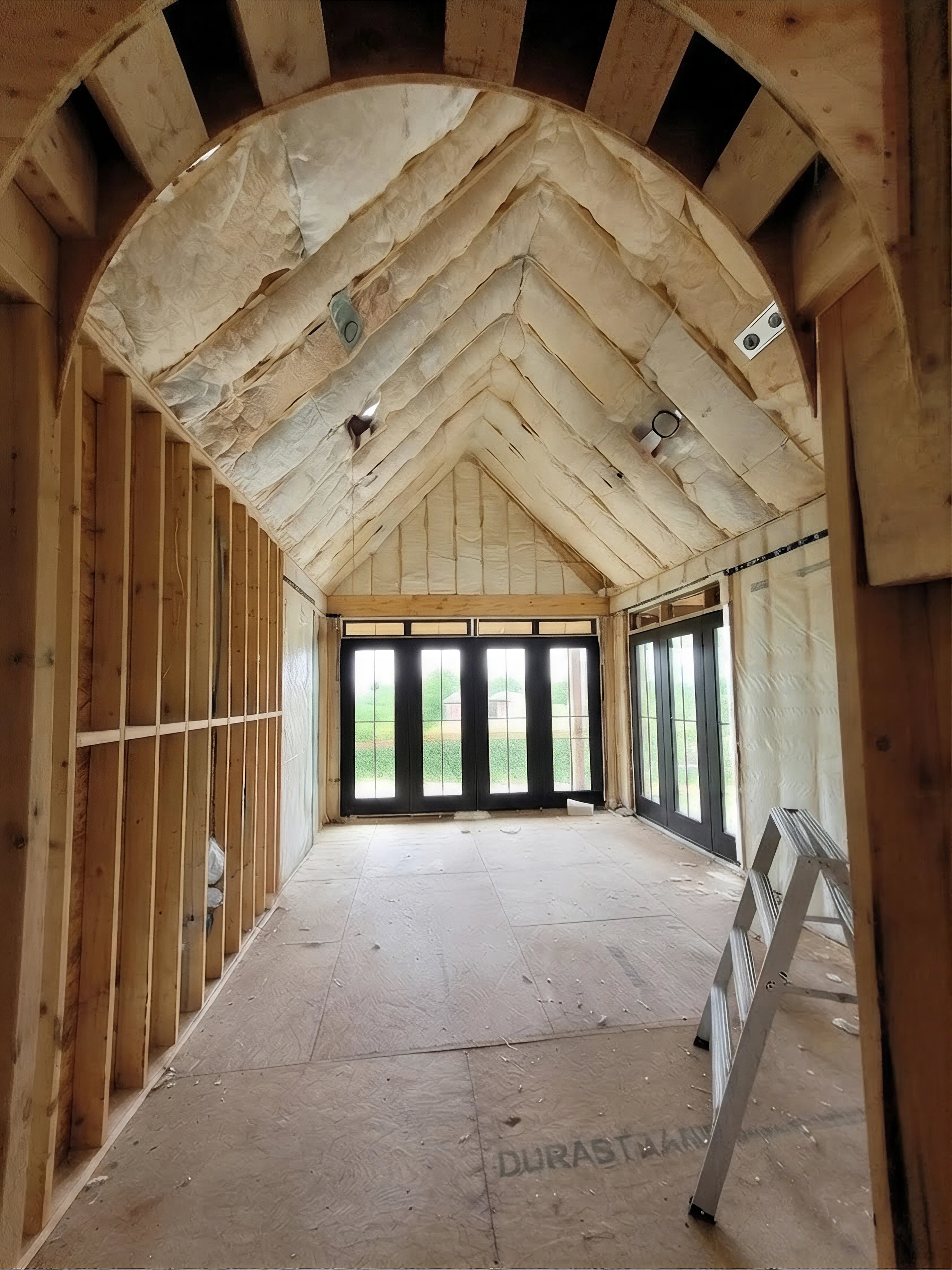 Inside of a house under construction showing insulation installed. There are glass doors also letting in a lot of sunlight and showing greenery in the back.