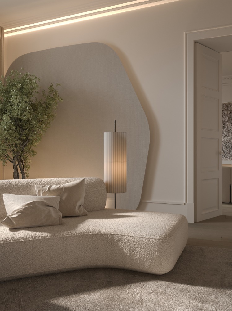 Minimalist beige living room corner with curved sofa, two cushions, a tall floor lamp, and a potted plant against a light wall panel.