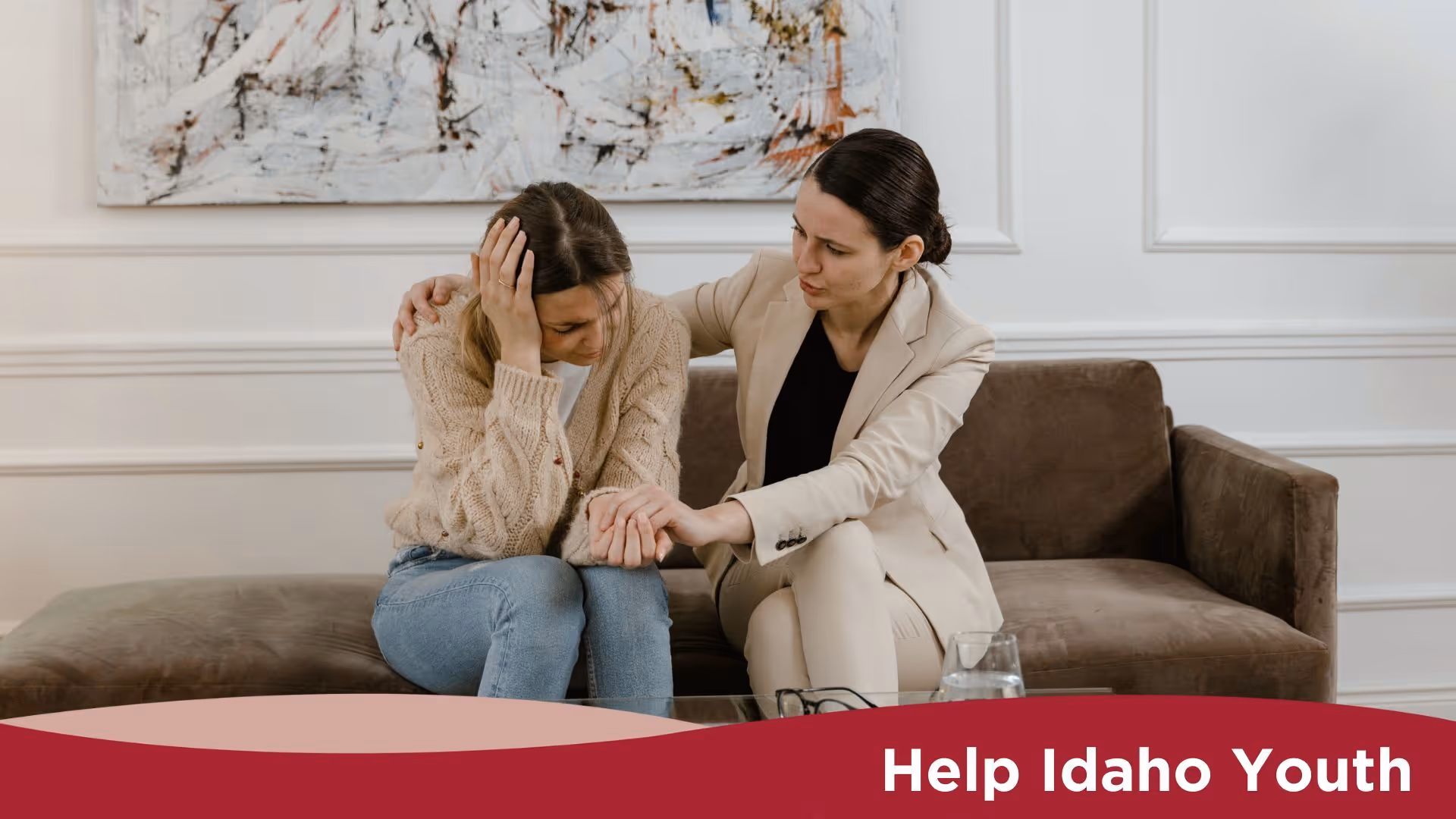 Two women sitting on a couch with one of them comforting the other. The text at the bottom of the image reads, "Help Idaho Youth."
