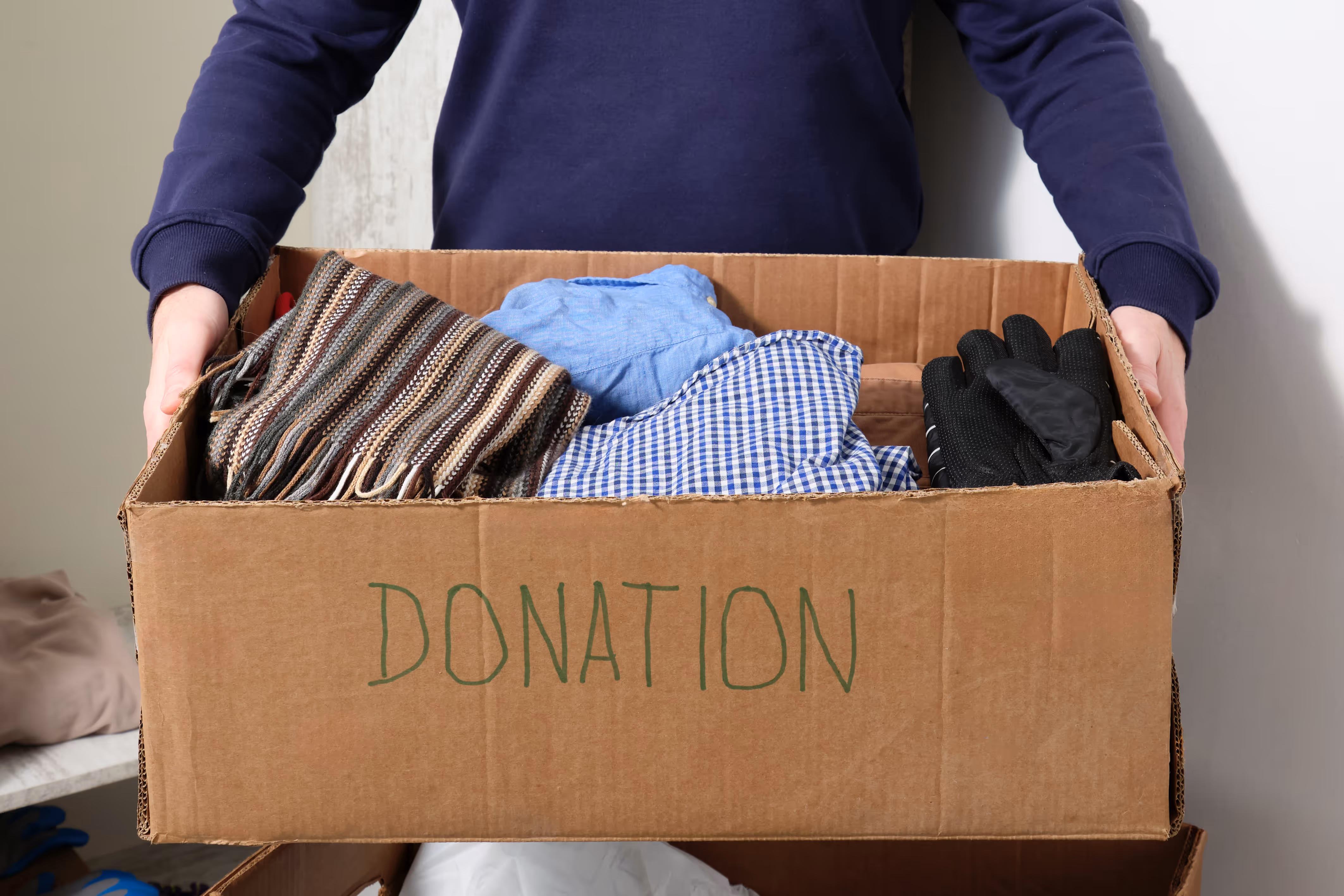 Person holding a donation box filled with clothes