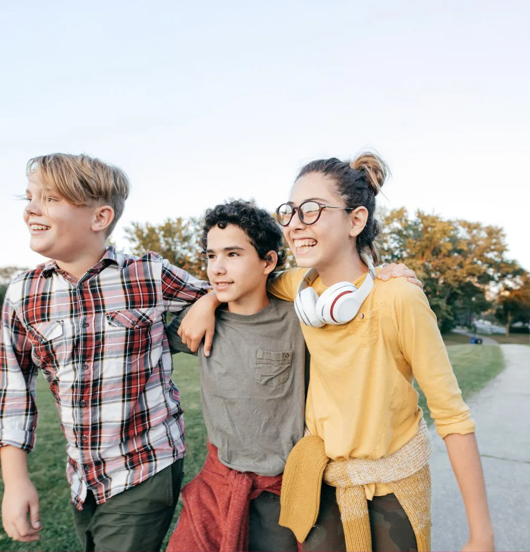3 smiling kids with arms linked walking down a concrete walkway