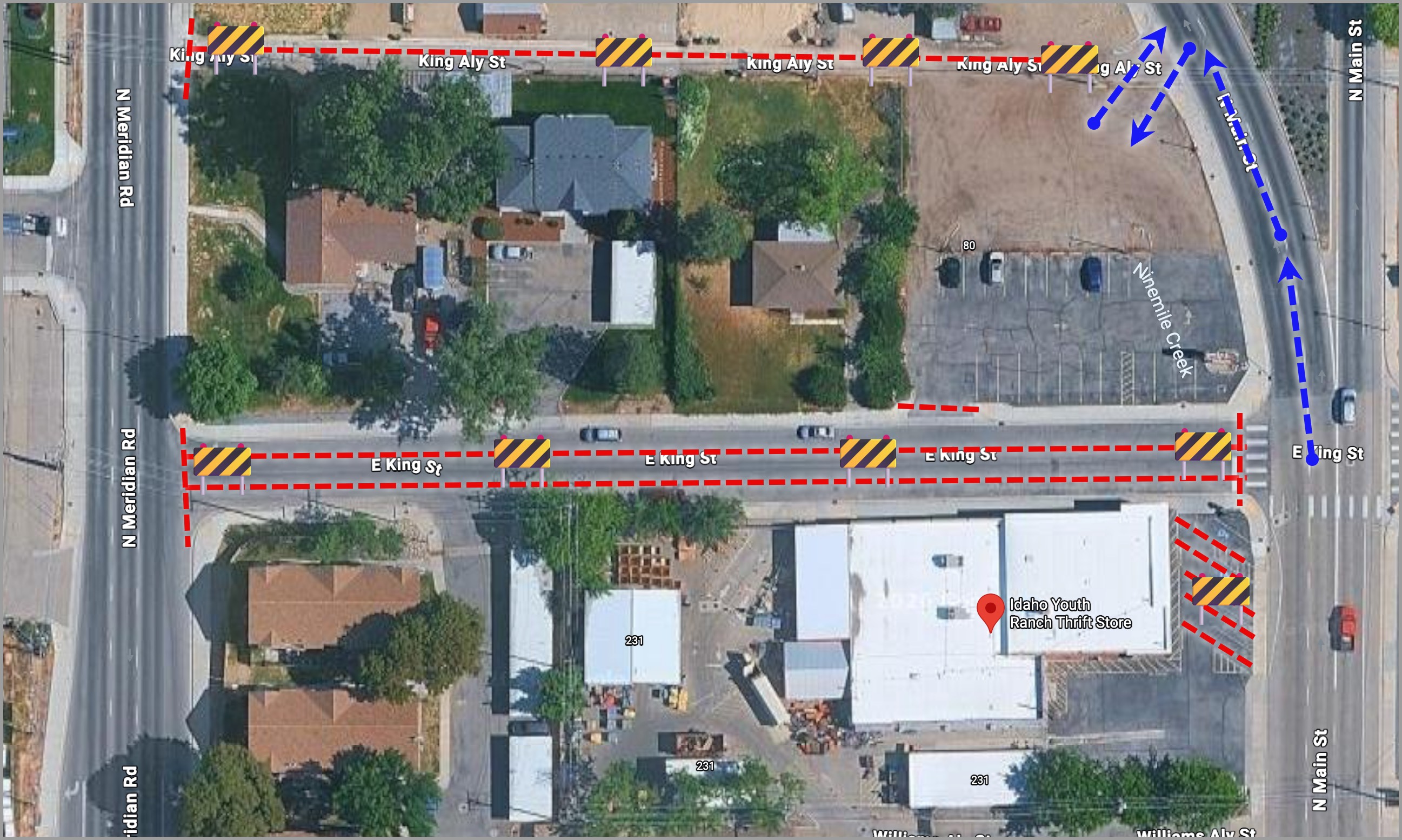 Aerial view of a city block showing street closures marked with red dashed lines and black-yellow barricades on King Aly St and E King St. Blue dashed arrows depict a detour path along N Main St. The Idaho Youth Ranch Thrift Store is located near the bottom right corner of the block.