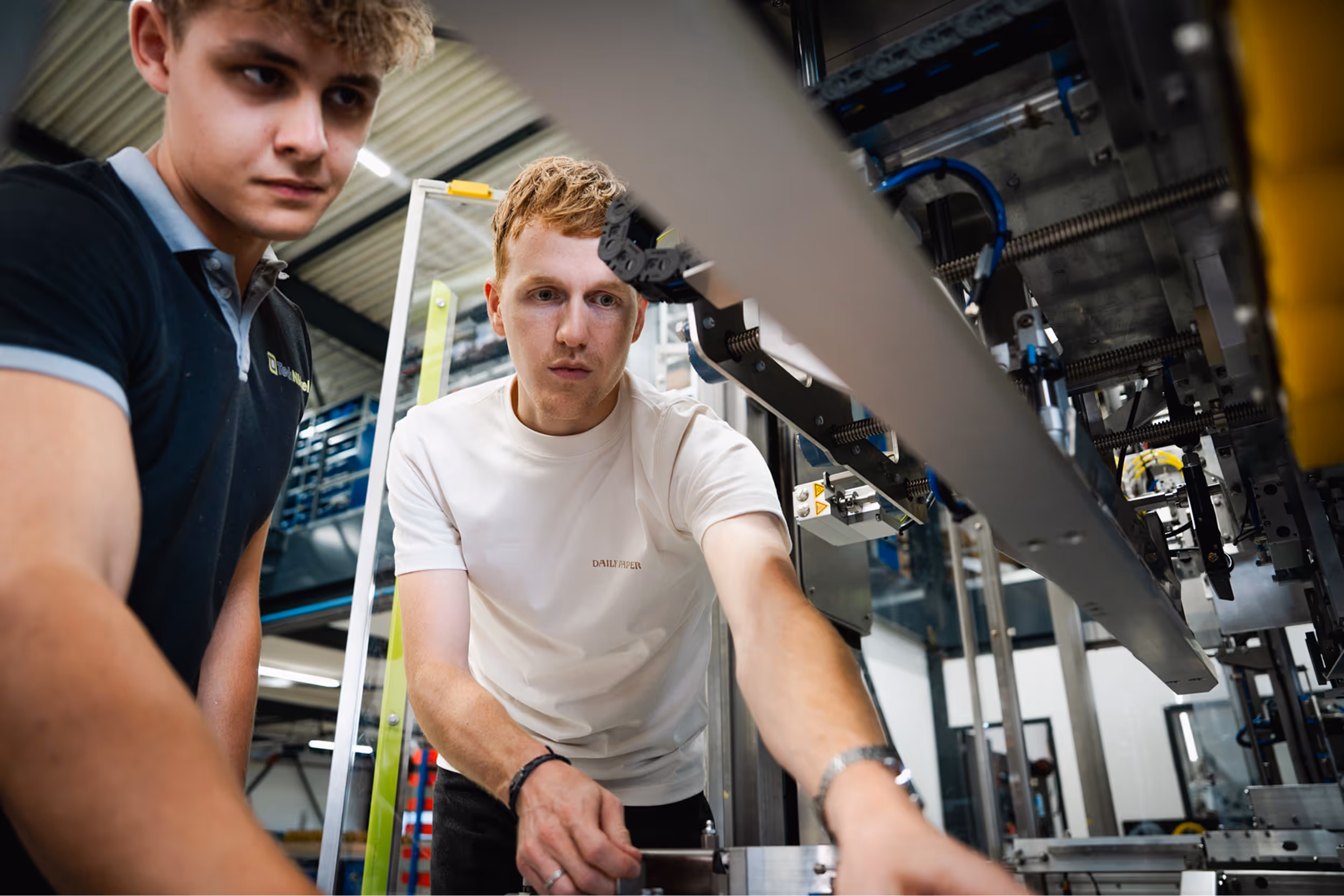 Twee jonge mannen die aandachtig aan een industriële machine in een fabriek werken.