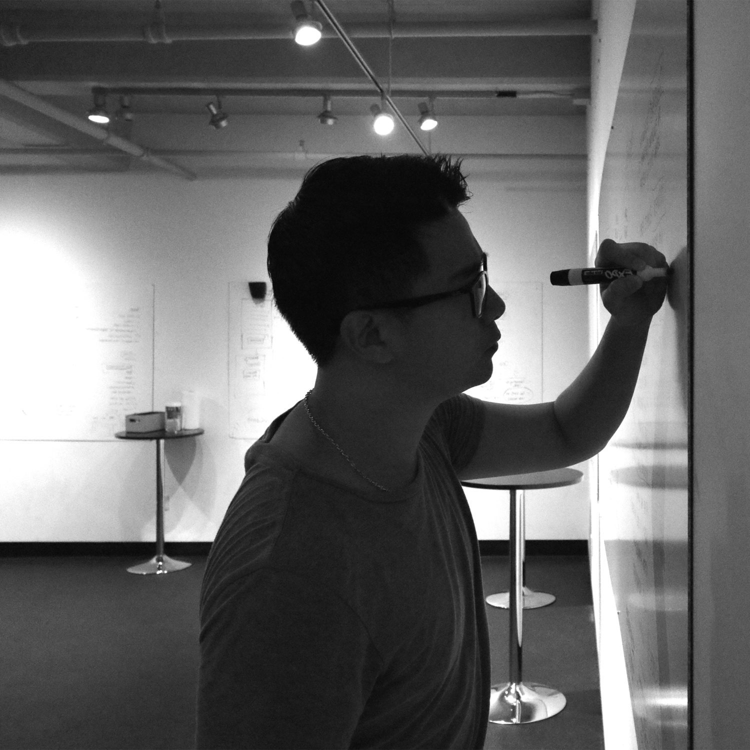 Man wearing glasses writing on a whiteboard in a modern office space.
