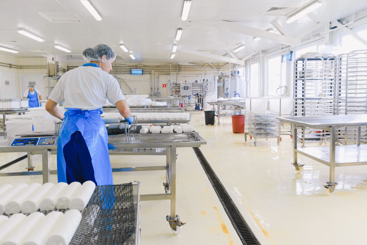 Bright hygienic food production hall with stainless steel tables, floor drainage, and workers in protective clothing