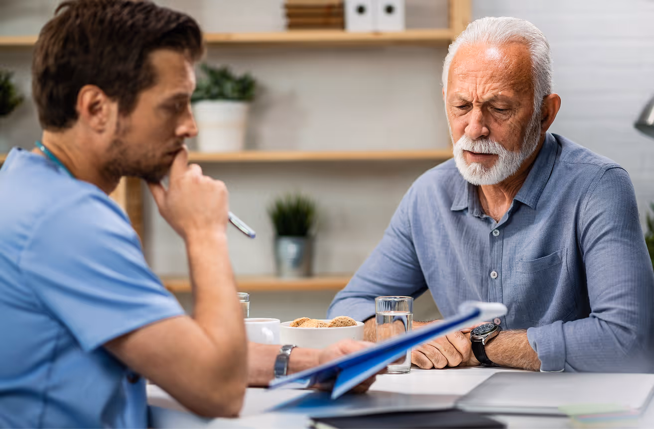 Elderly man with white hair and beard looking concerned during a consultation with a male medical professional.