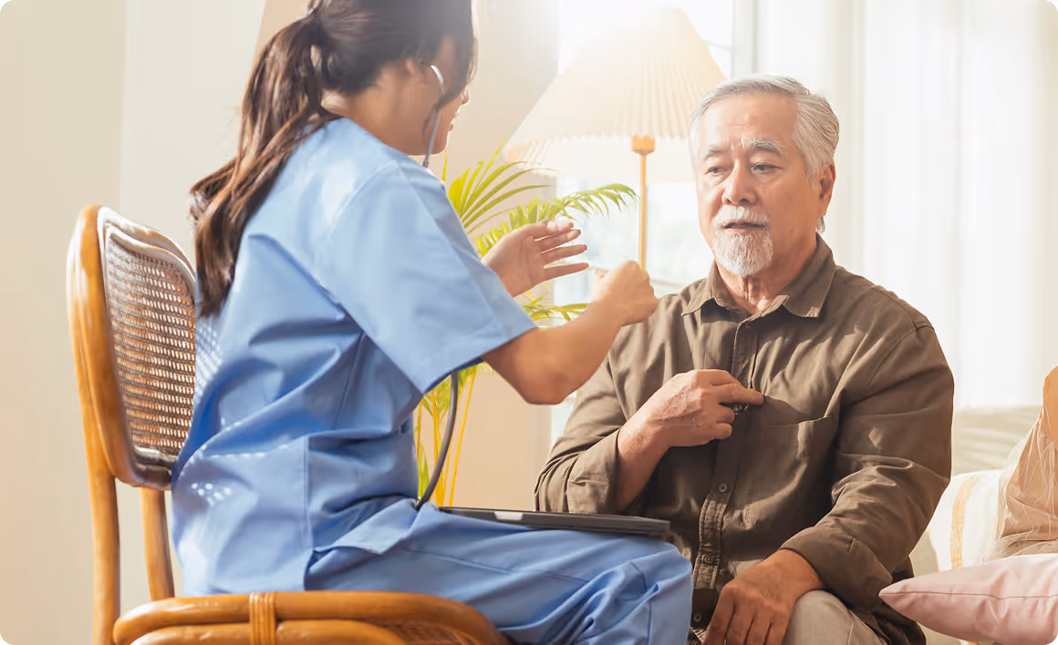 Healthcare professional in blue scrubs using a stethoscope to check an elderly man's heartbeat.