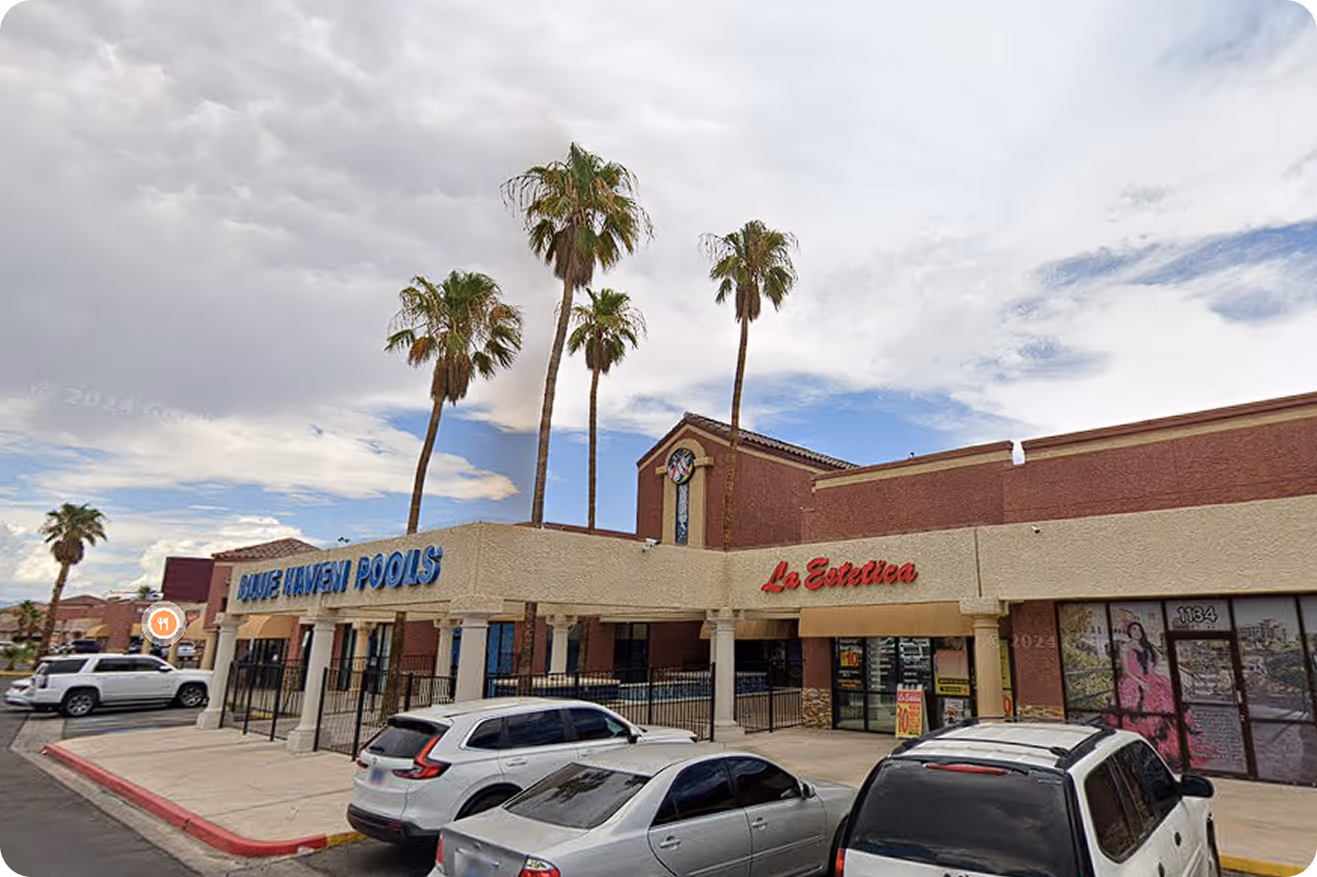 Shopping center with stores Blue Haven Pools and La Estetica, palm trees, and parked cars under a cloudy sky.