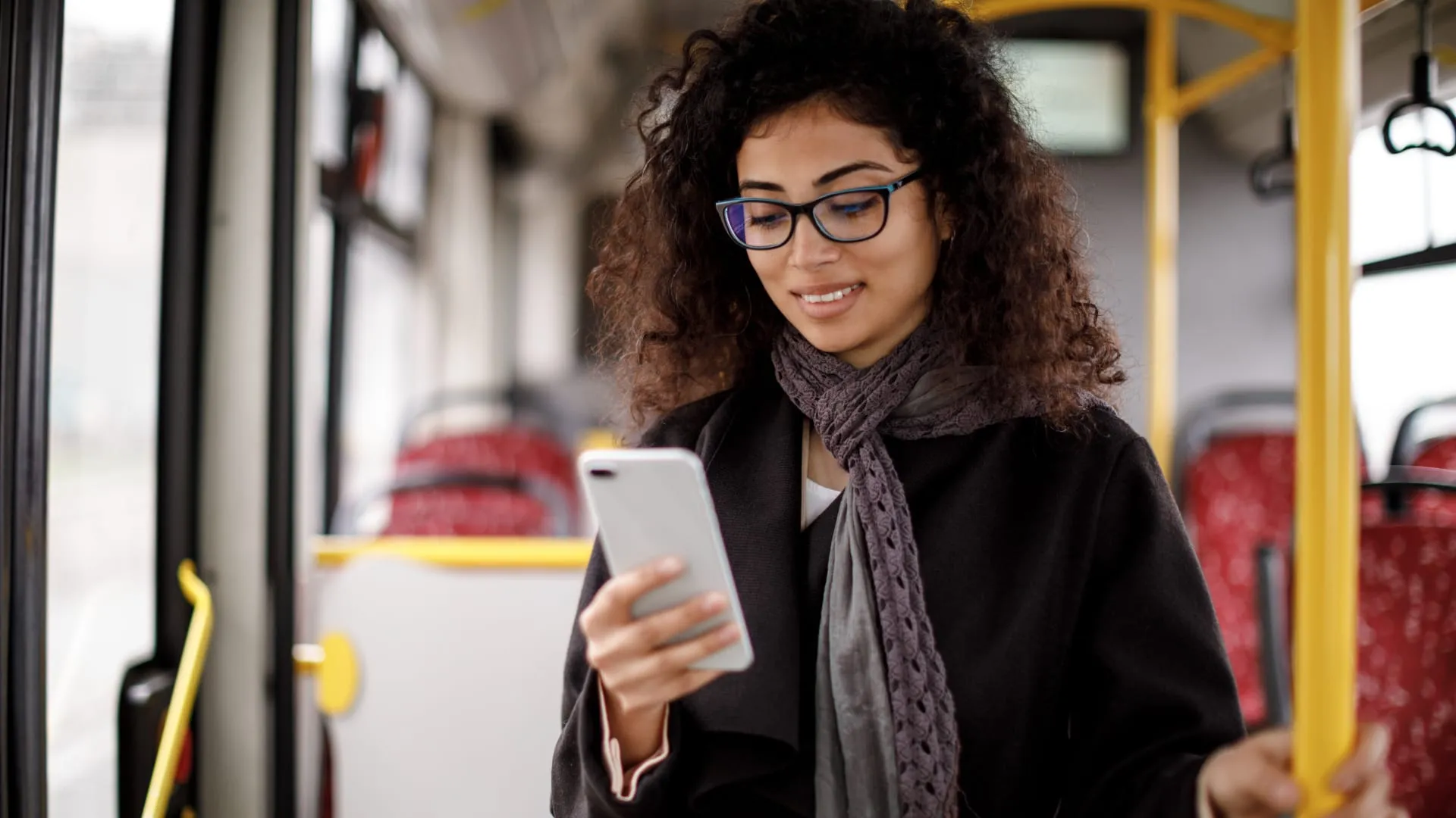 Une femme dans un autobus avec un téléphone cellulaire en main.
