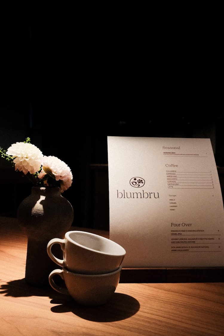 Two small cups of coffee stacked on top of each other next to flowers and a blumbru menu.