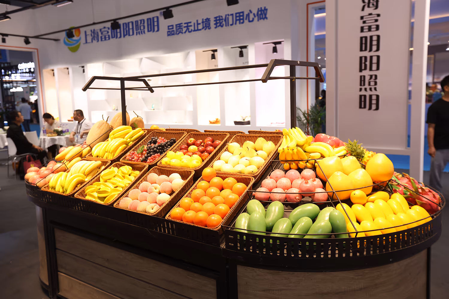 Market stall displaying baskets of assorted fresh fruits including bananas, grapes, apples, oranges, pomegranates, and pears indoors.