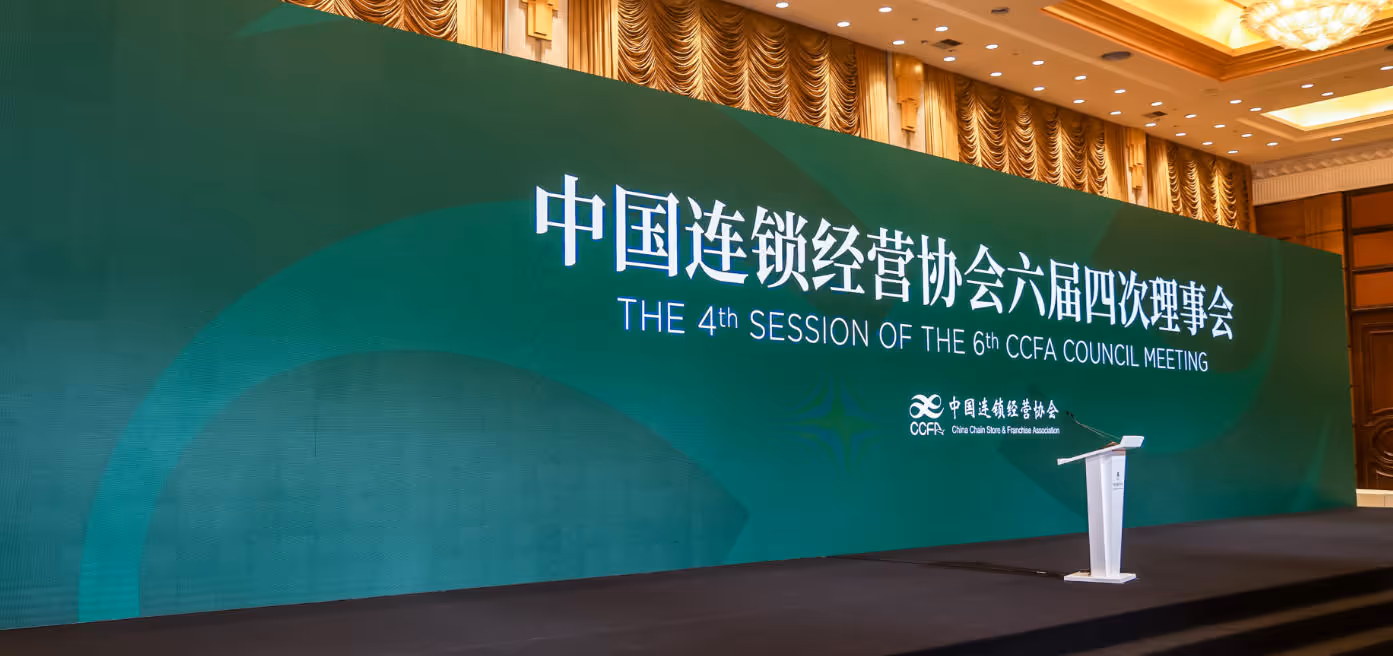 Large green backdrop at a conference hall displaying text for the 4th session of the 6th CCFA council meeting with a white podium on stage.