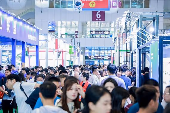 Crowded indoor convention or trade show with many people walking and browsing booths.
