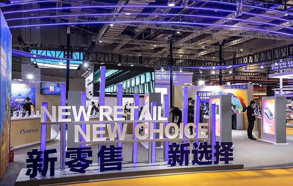 Exhibition booth with illuminated sign reading 'NEW RETAIL | NEW CHOICE' in English and Chinese, featuring digital displays and attendees.