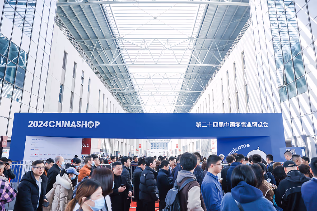 Crowd of people entering the 2024 CHINASHOP retail exhibition under a large blue banner inside a bright, modern hall.