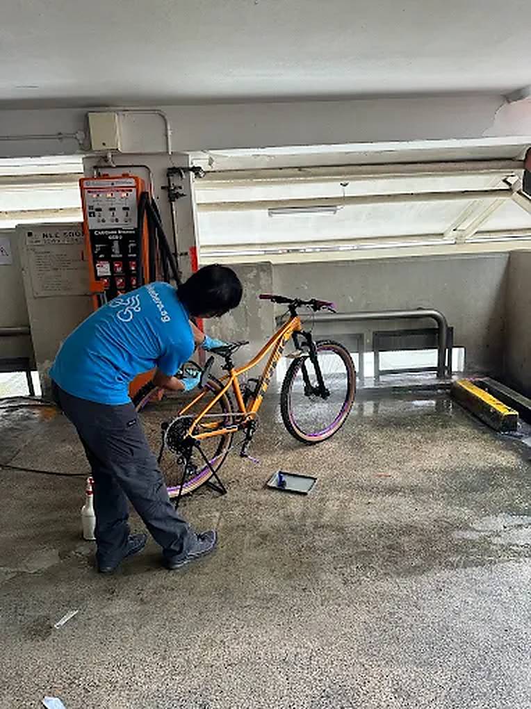 Bike Hero mechanic servicing an orange mountain bike at an HDB void deck
