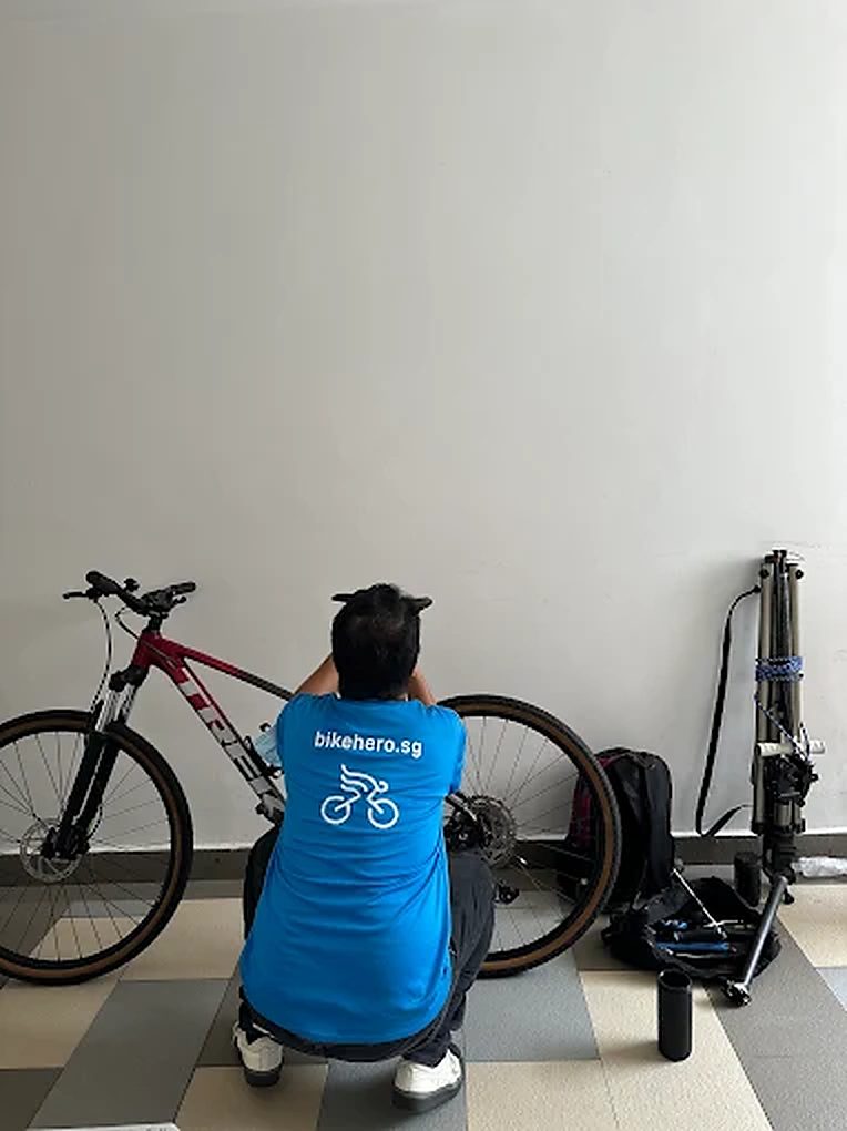 Bike Hero mechanic in a bikehero.sg shirt working on a mountain bike on site