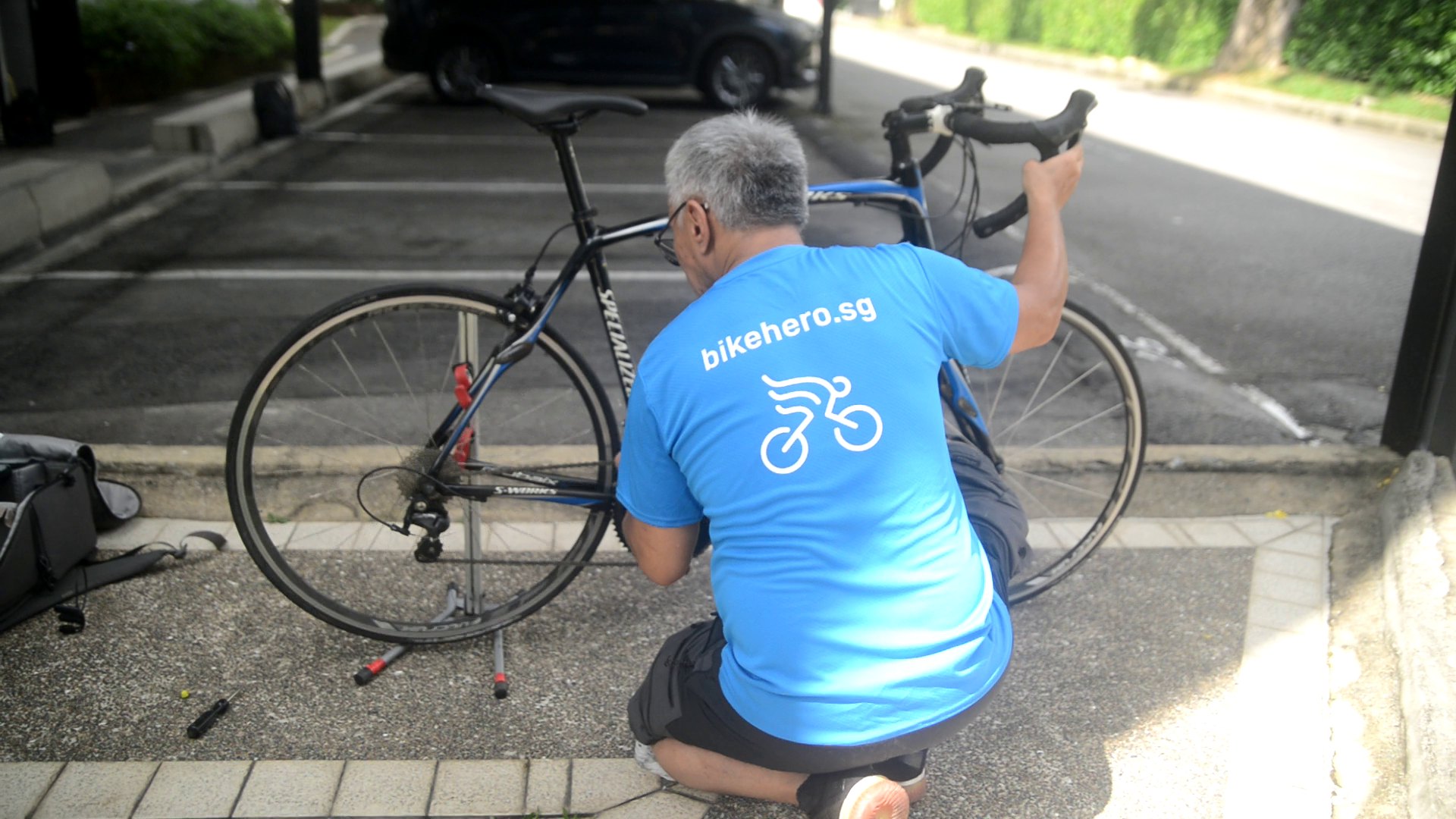 Bike Hero mechanic servicing a road bike in a Singapore car park, with tools and work stand set up on the kerb