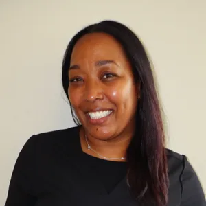 Smiling woman with long dark hair wearing a black top against a plain light background.