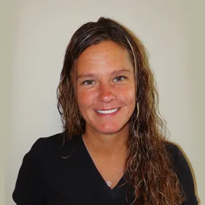 Smiling woman with long, wavy brown hair wearing a black top against a plain background.