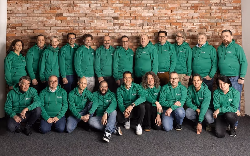 Gruppenfoto des Ipex-Teams, alle tragen grüne Kapuzenpullover mit dem Ipex-Logo vor einer Backsteinwand.