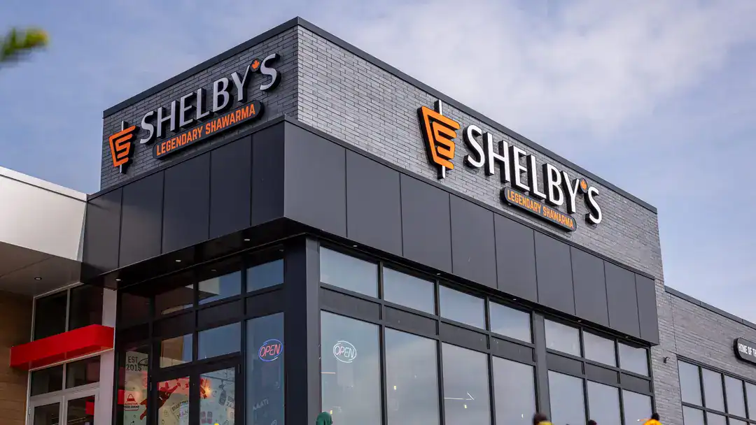 Exterior view of Shelby's Legendary Shawarma restaurant with black and gray exterior and illuminated open signs on glass windows.