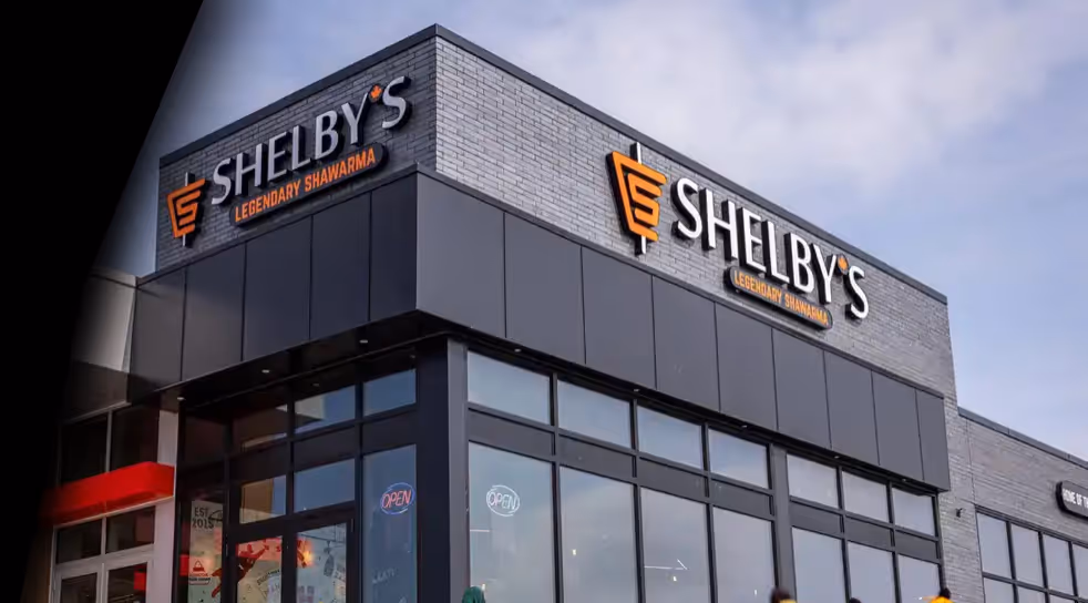 Exterior view of Shelby's Legendary Shawarma restaurant with large glass windows and illuminated open signs.