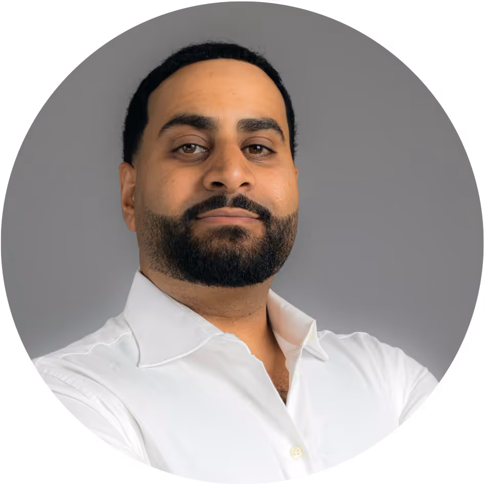 Portrait of a confident man with a beard wearing a white shirt against a gray background.