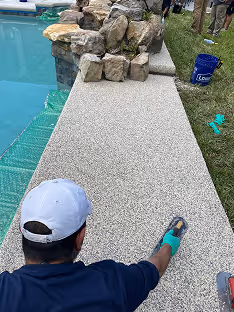 Worker installing a resin bound stone walkway beside a backyard pool