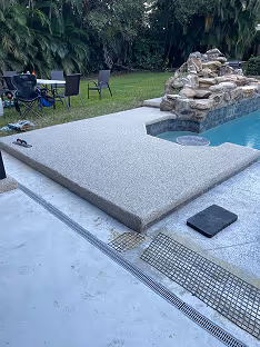 Resin bound stone pool edge and deck beside a backyard pool with a rock water feature