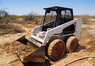 Skid-steer loader digging dry dirt in a desert landscape.