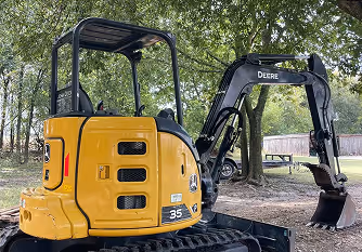 Yellow John Deere 35 excavator parked on dirt under trees with a picnic table in the background.