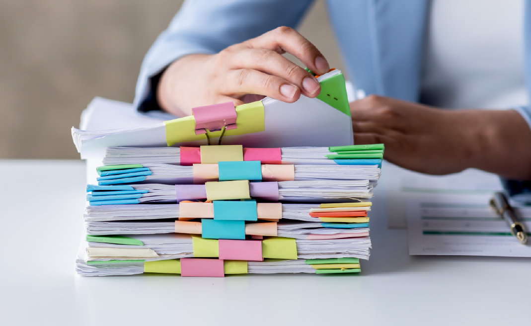 Person organizing a thick stack of documents with colorful binder clips and tabs on a white desk.