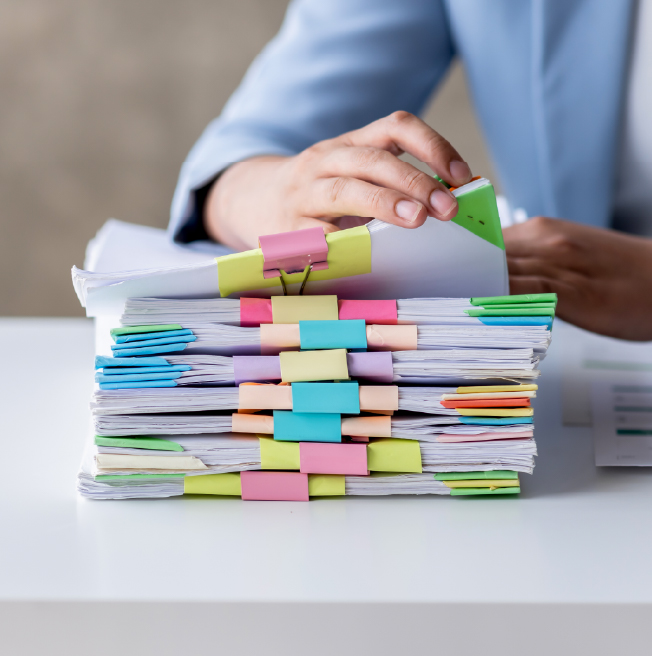Person organizing large stack of documents with colorful paper clips and tabs on white desk.