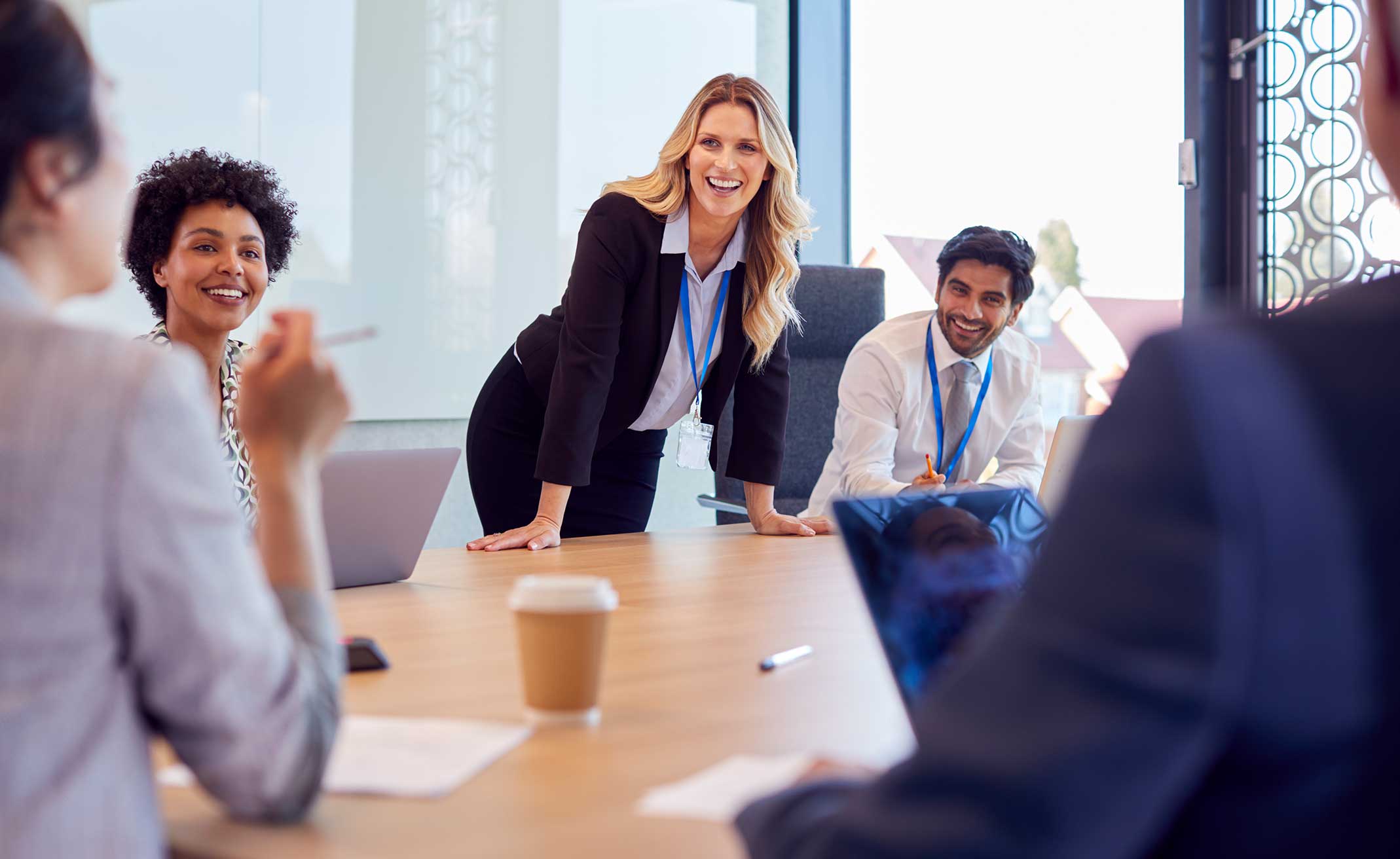 Business people having a meeting around a glass table with a woman in white leading the discussion.