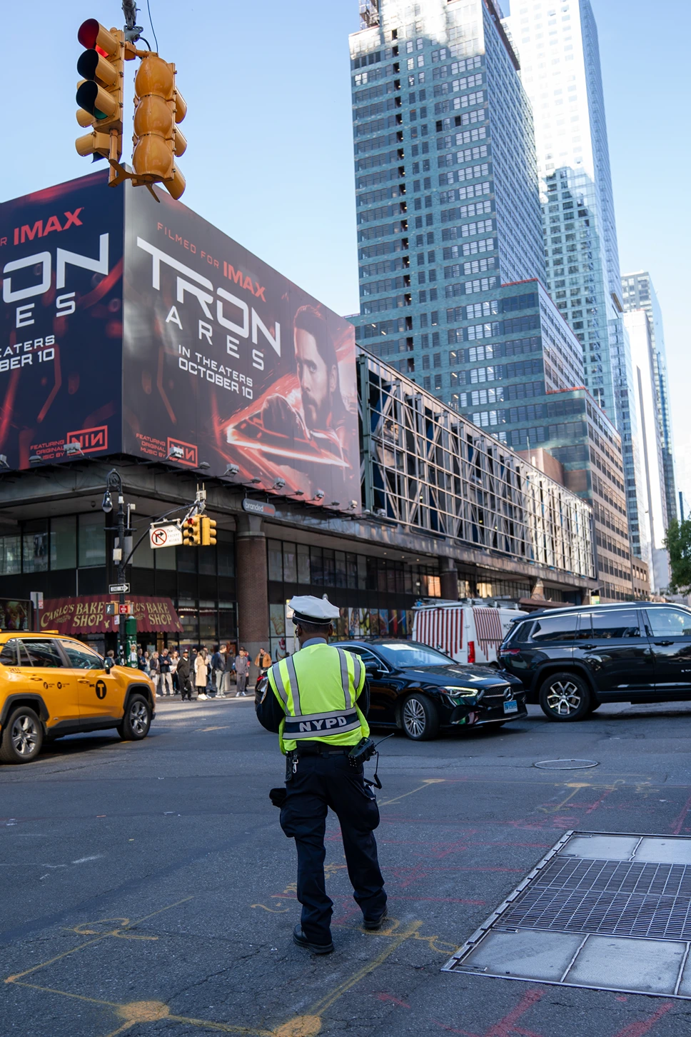 NYPD officer directing traffic at a busy city intersection with a large billboard for the movie Tron Ares in the background.