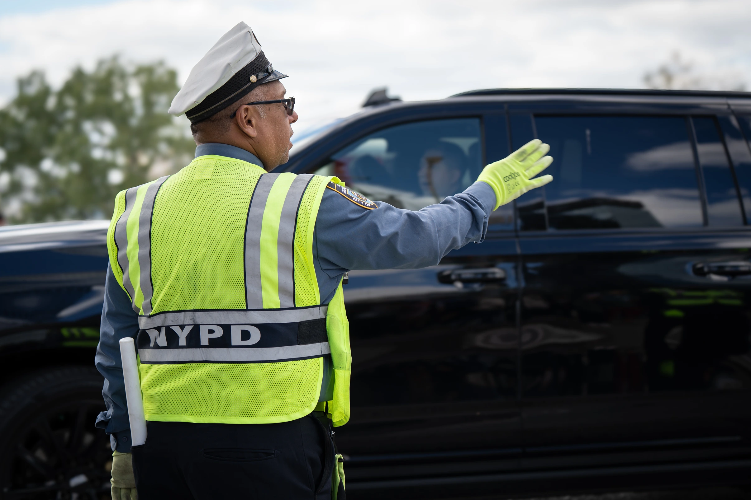 NYPD officer in a high-visibility vest directing traffic beside a black vehicle.