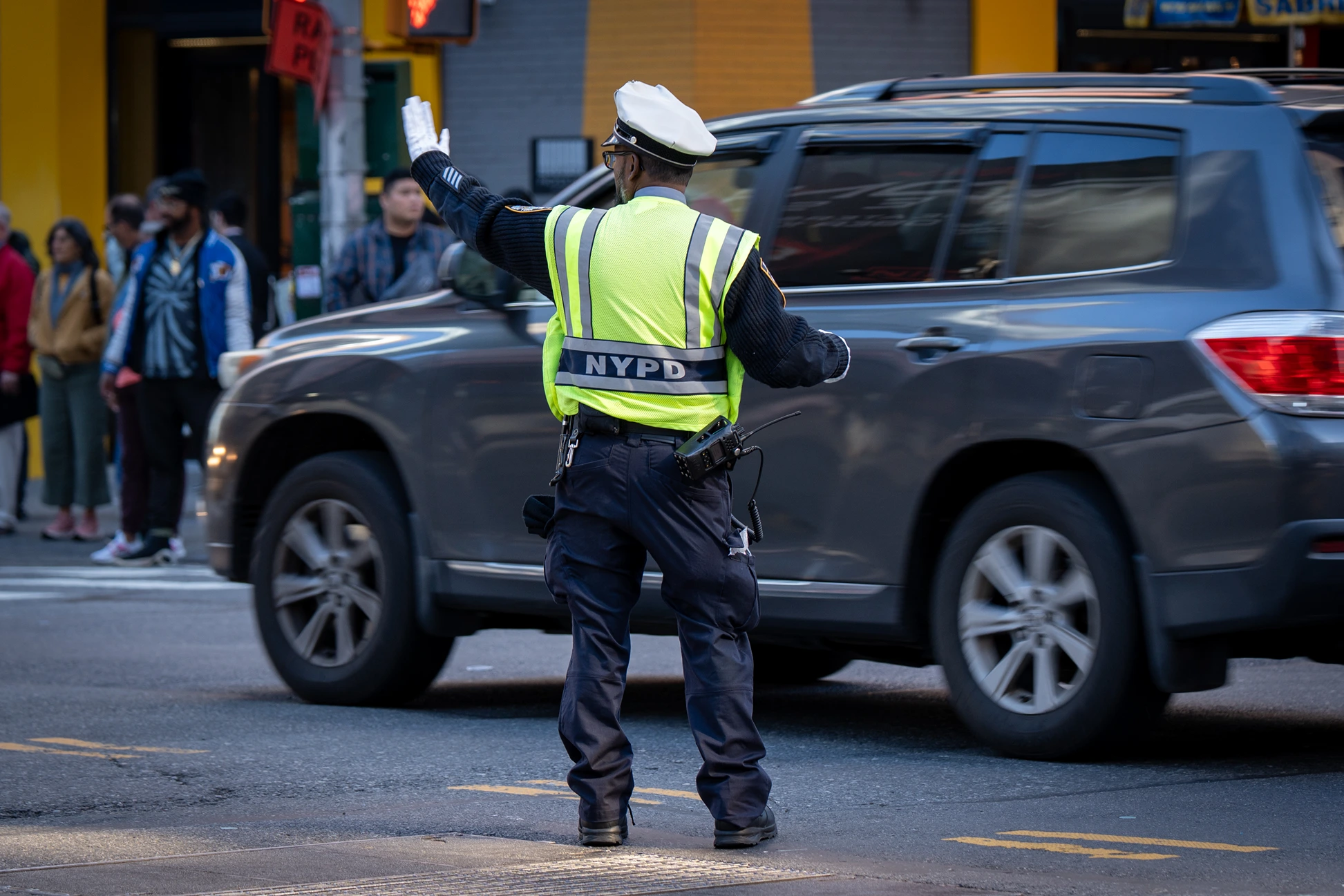 NYPD traffic officer wearing a high-visibility vest directing vehicles at a busy city street intersection.
