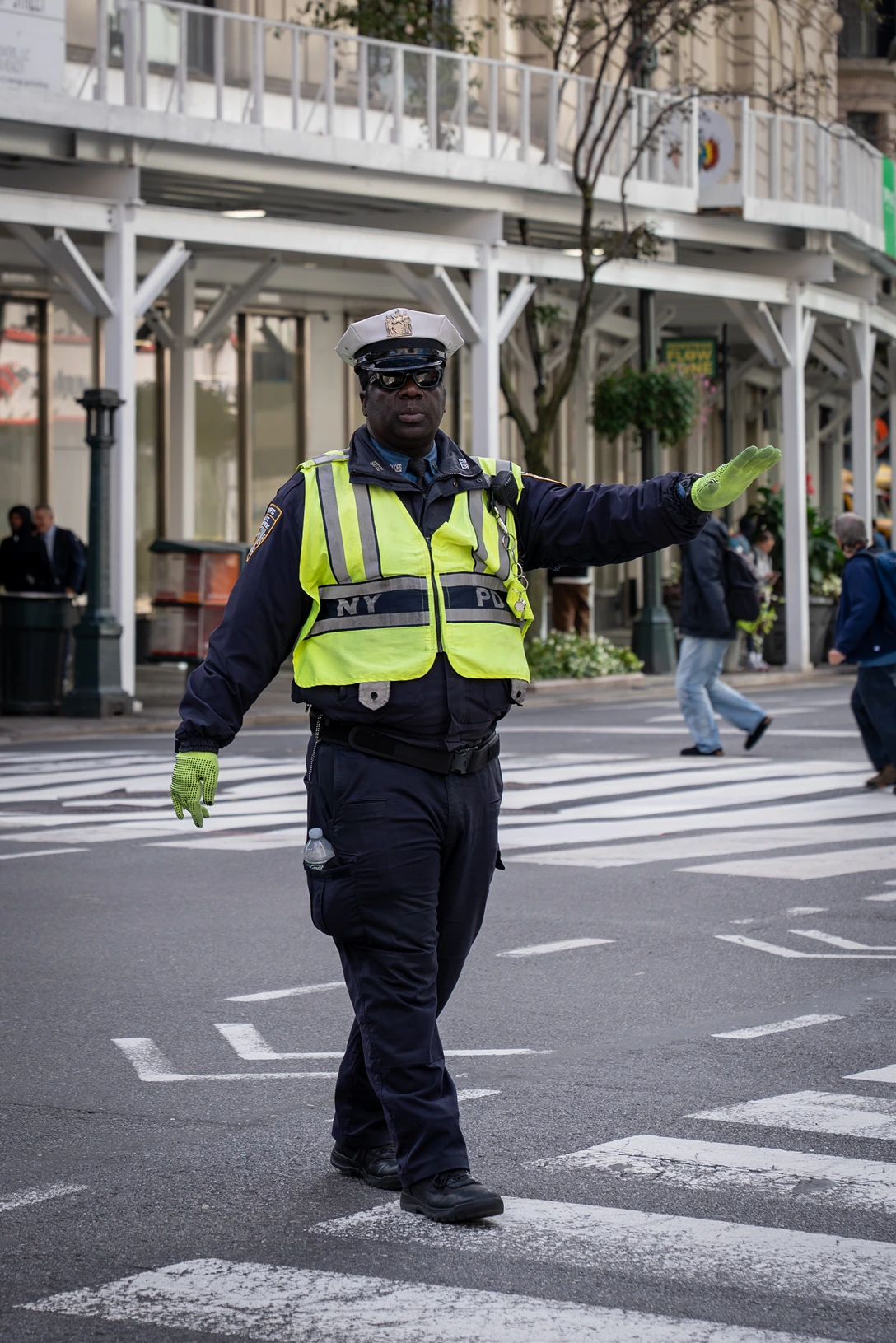 NYPD police officer wearing a reflective yellow vest and neon green gloves directing traffic on a city street.