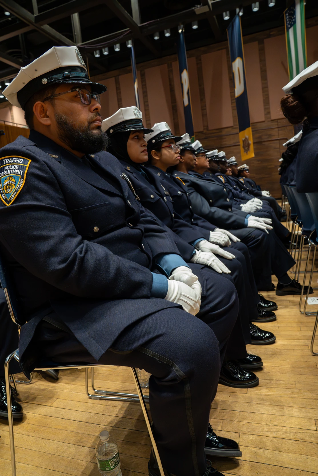 Row of uniformed NYPD traffic police officers seated indoors, wearing white gloves and hats.