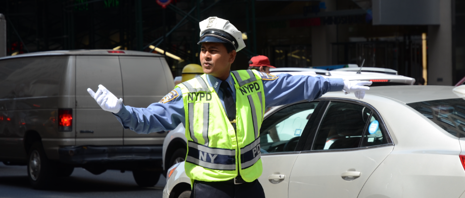 NYPD traffic officer in uniform directing vehicles on a busy city street.