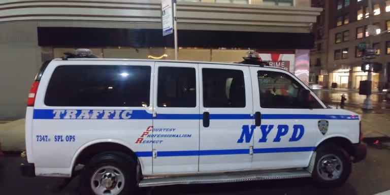 White NYPD traffic van parked on a city street at night with blue stripes and police decals.