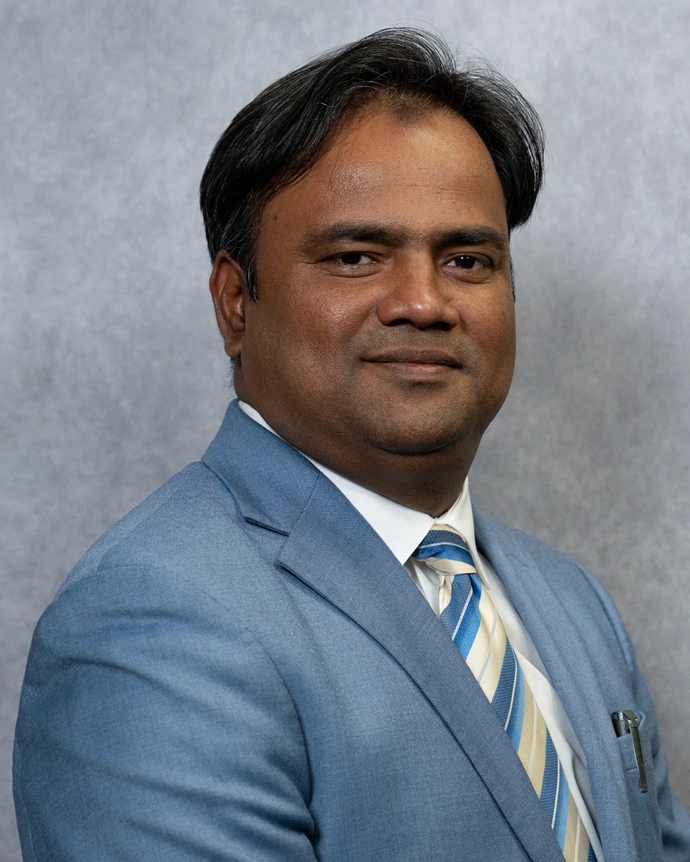 Portrait of a man wearing a light blue suit jacket, white shirt, and striped tie against a gray background.