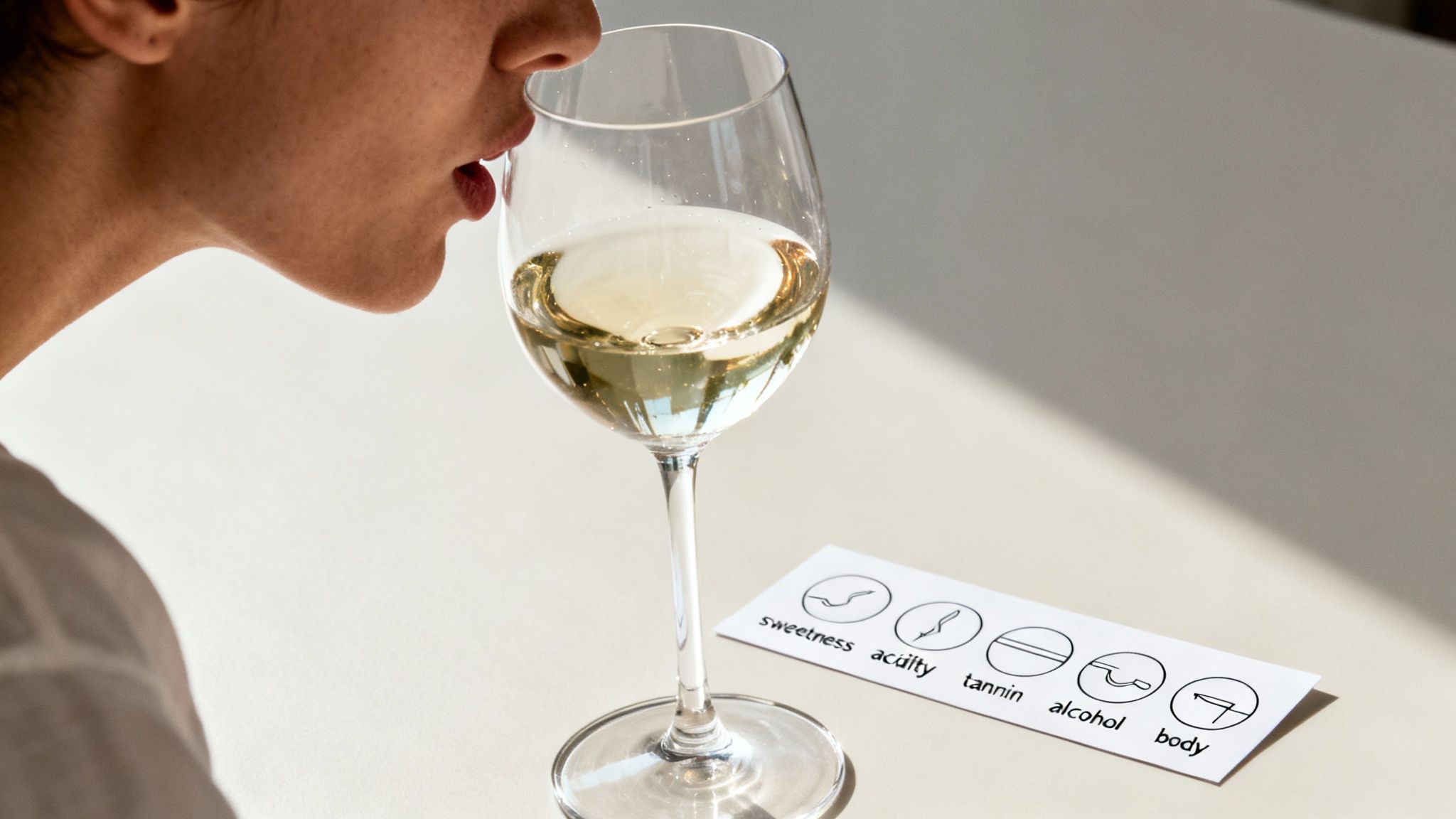 Woman smelling white wine in a glass with a tasting notes card showing sweetness and acidity.