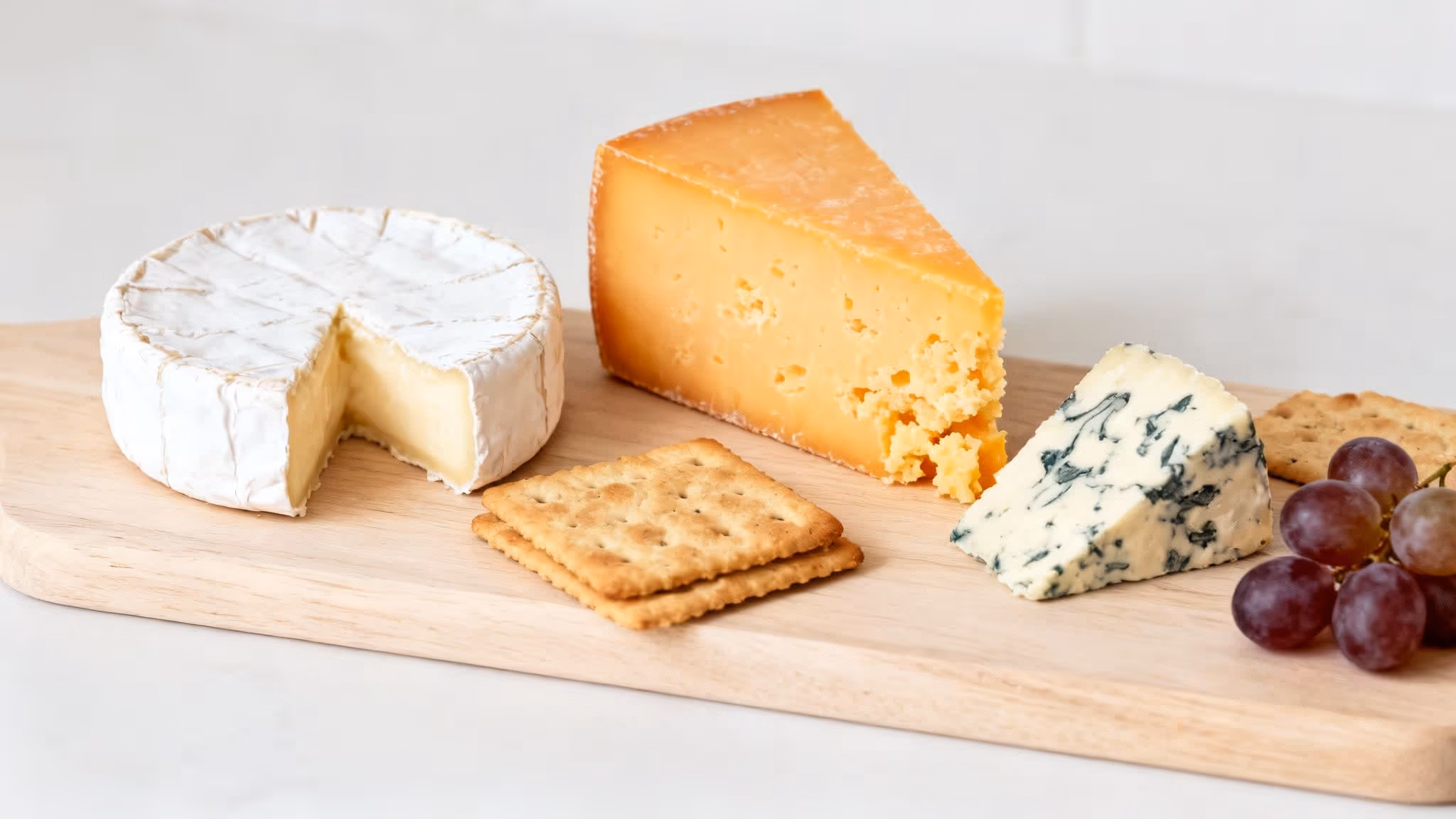Delicious cheese board with Camembert, Cheddar, blue cheese, crackers, and red grapes.