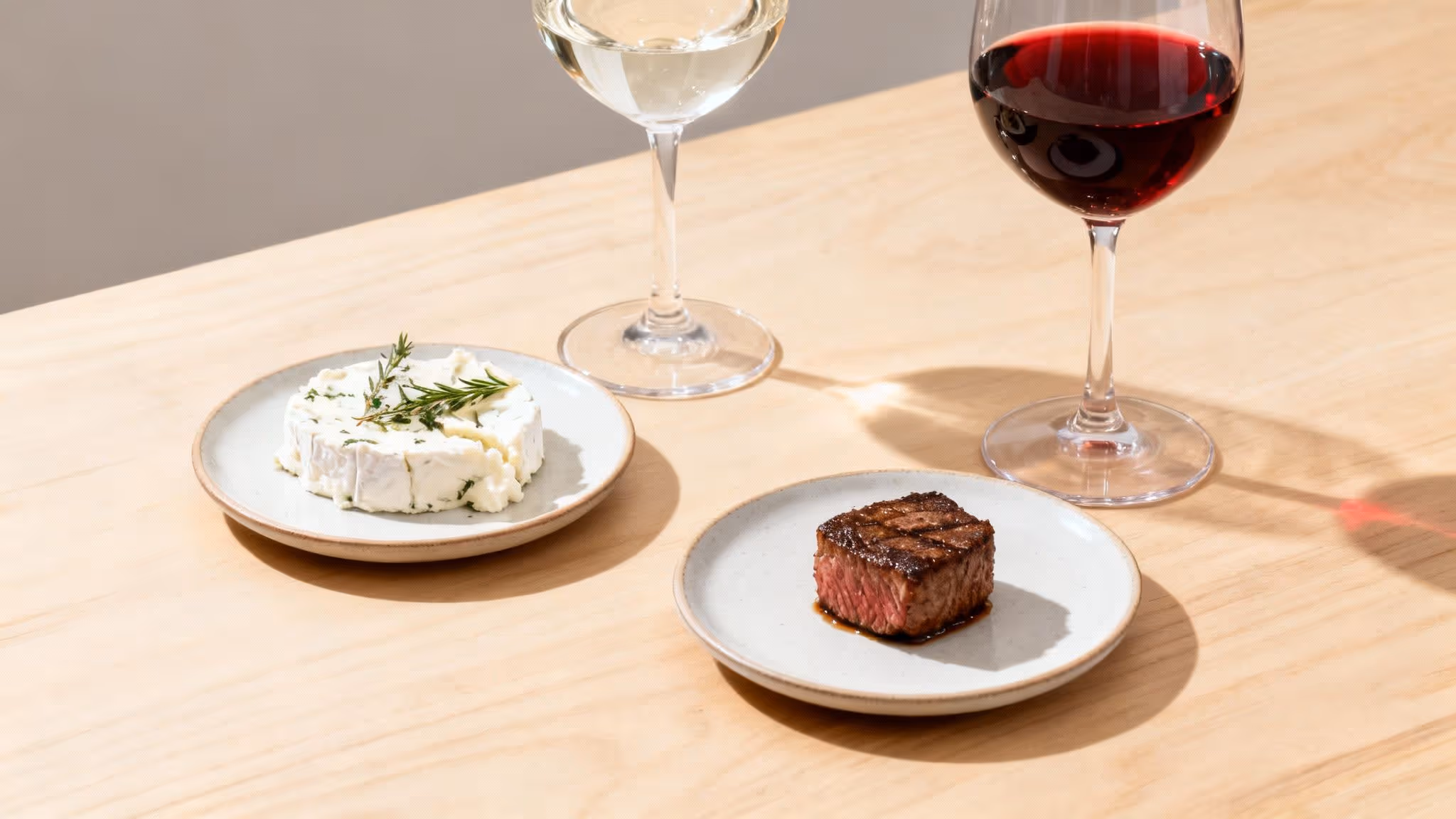 Two glasses of wine, white and red, served with cheese and steak on a wooden table.