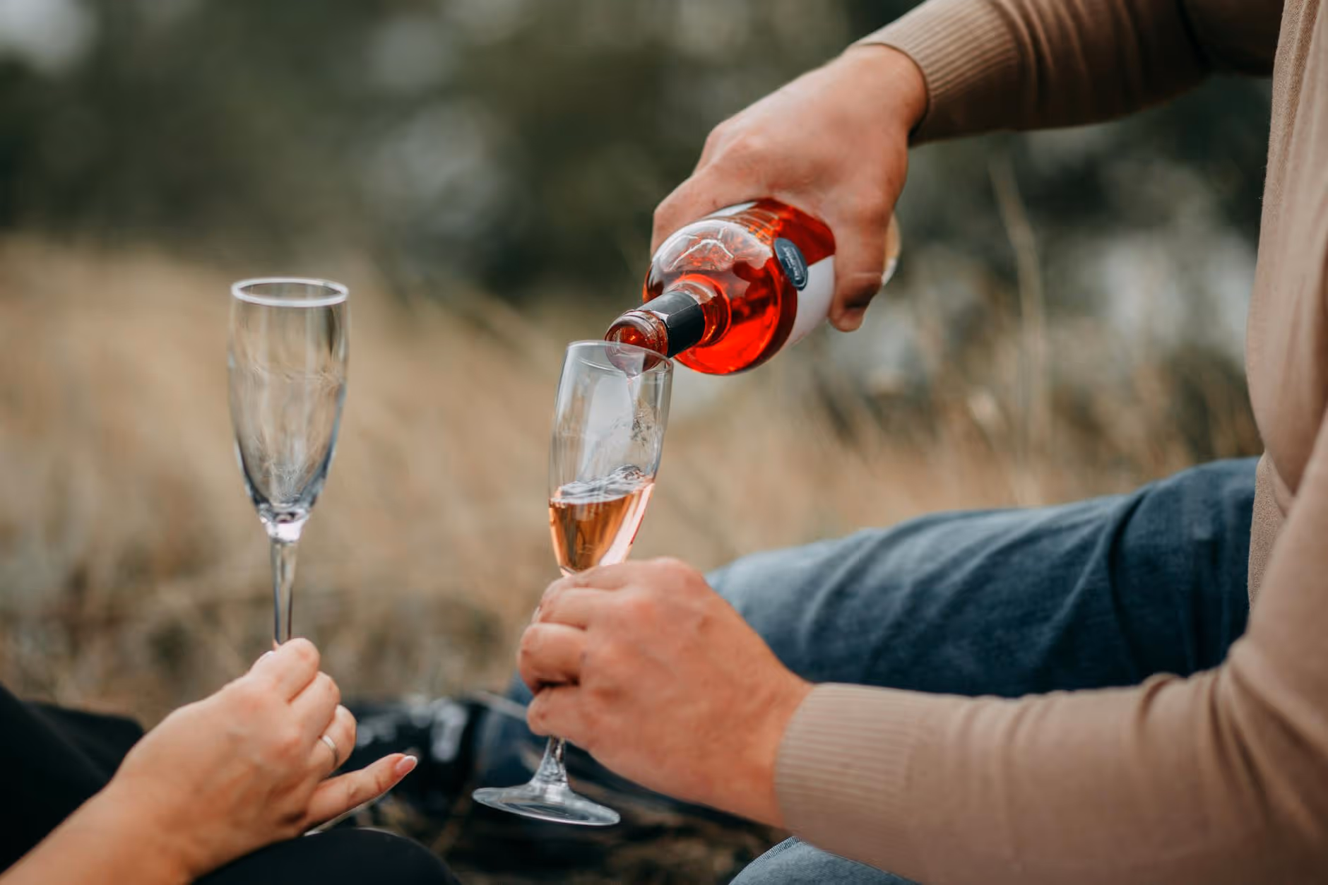 A couple enjoys a romantic outdoor moment, pouring rose wine into elegant glasses.