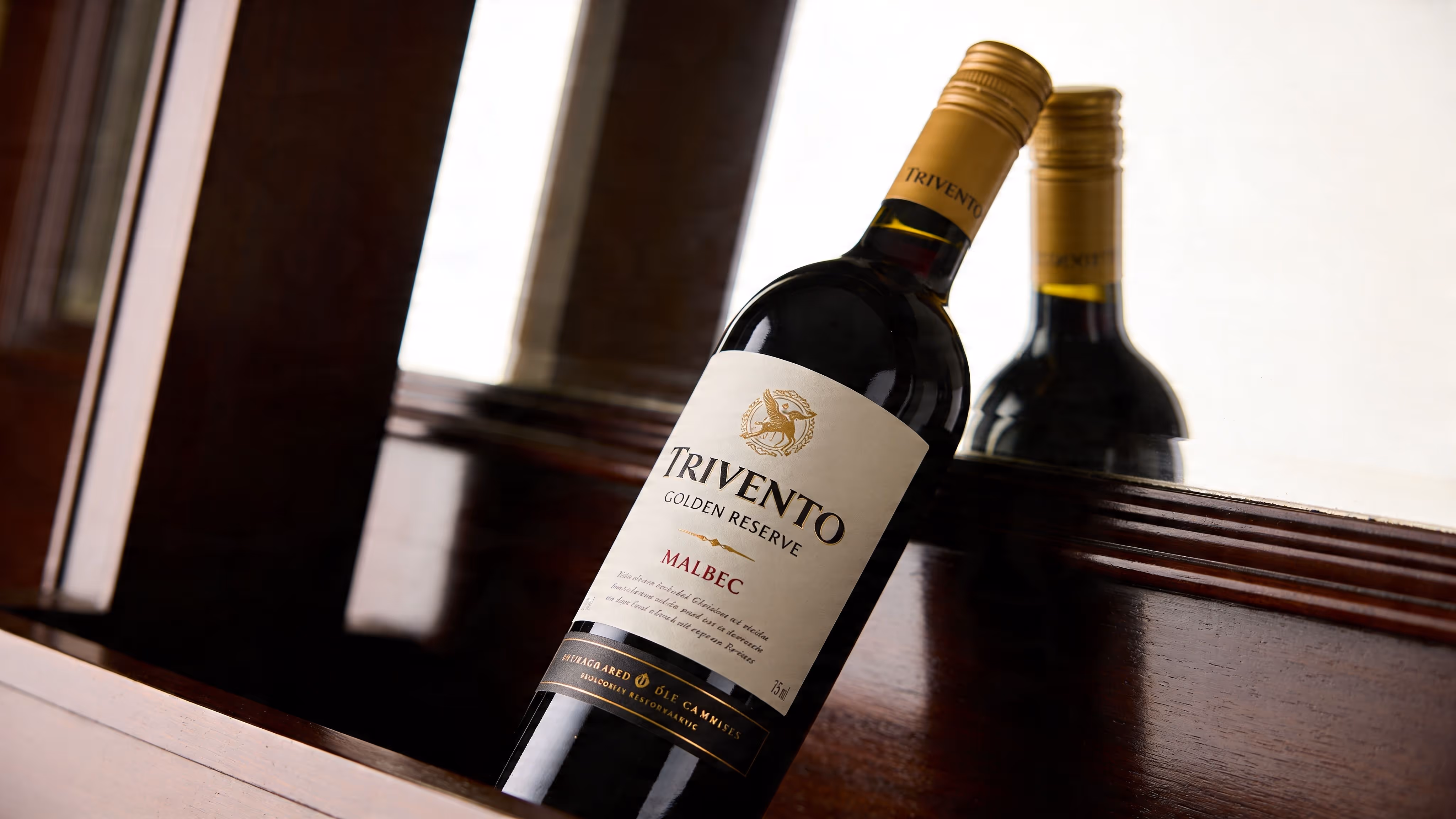 A bottle of Trivento Golden Reserve Malbec wine stands elegantly against a dark wooden surface with reflections.