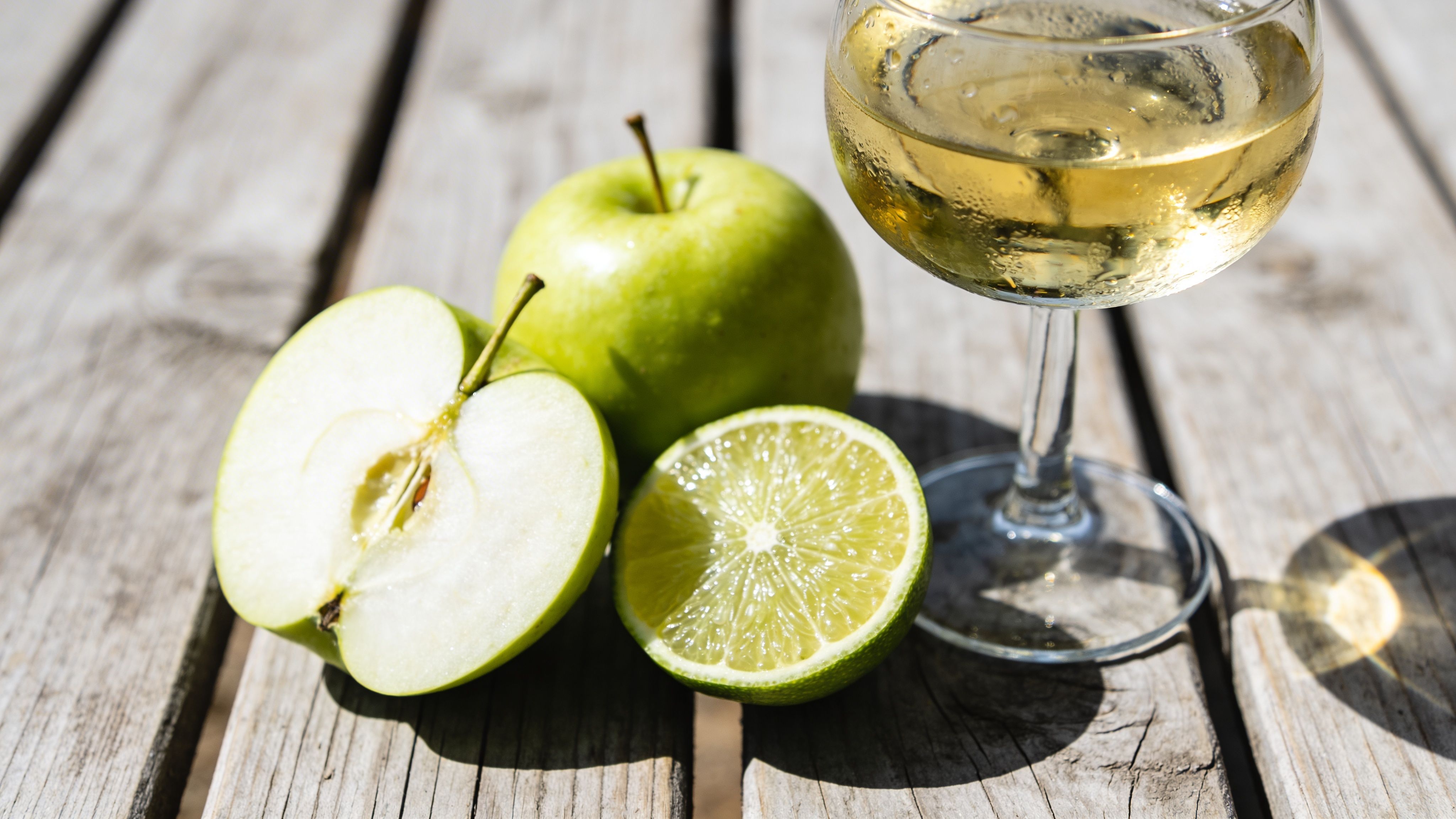 A glass of crisp white wine served next to fresh green apples and a cut lime.